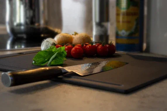 Nachhaltiges Schneidebrett mit frischen Tomaten, Basilikum und Küchenmesser in der Küche